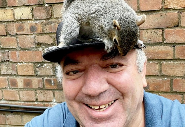 A man with a squirrel that he rescued sitting on his head.